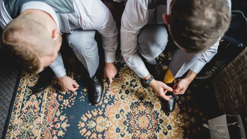 Groomsmen tying shoelaces on an old rug at Grittleton House