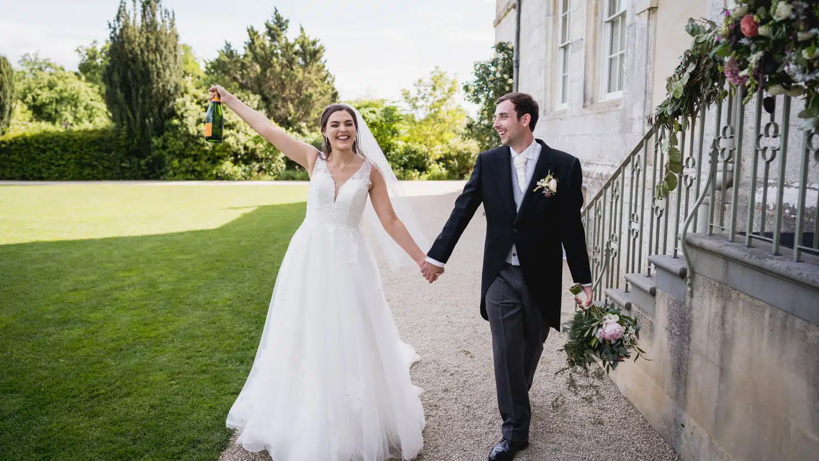 Newlyweds walking past the stone steps and gardens of Elmore Court