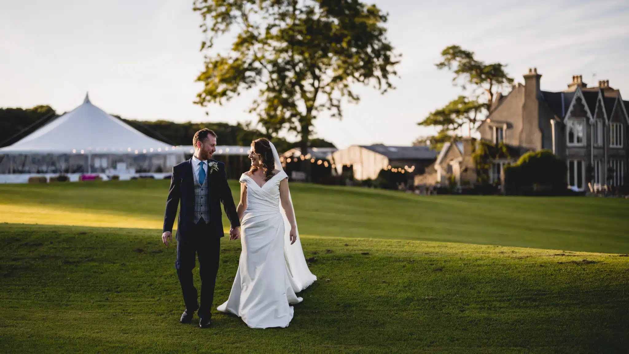 Couple walking across the lawn with a sailcloth tent and country house behind