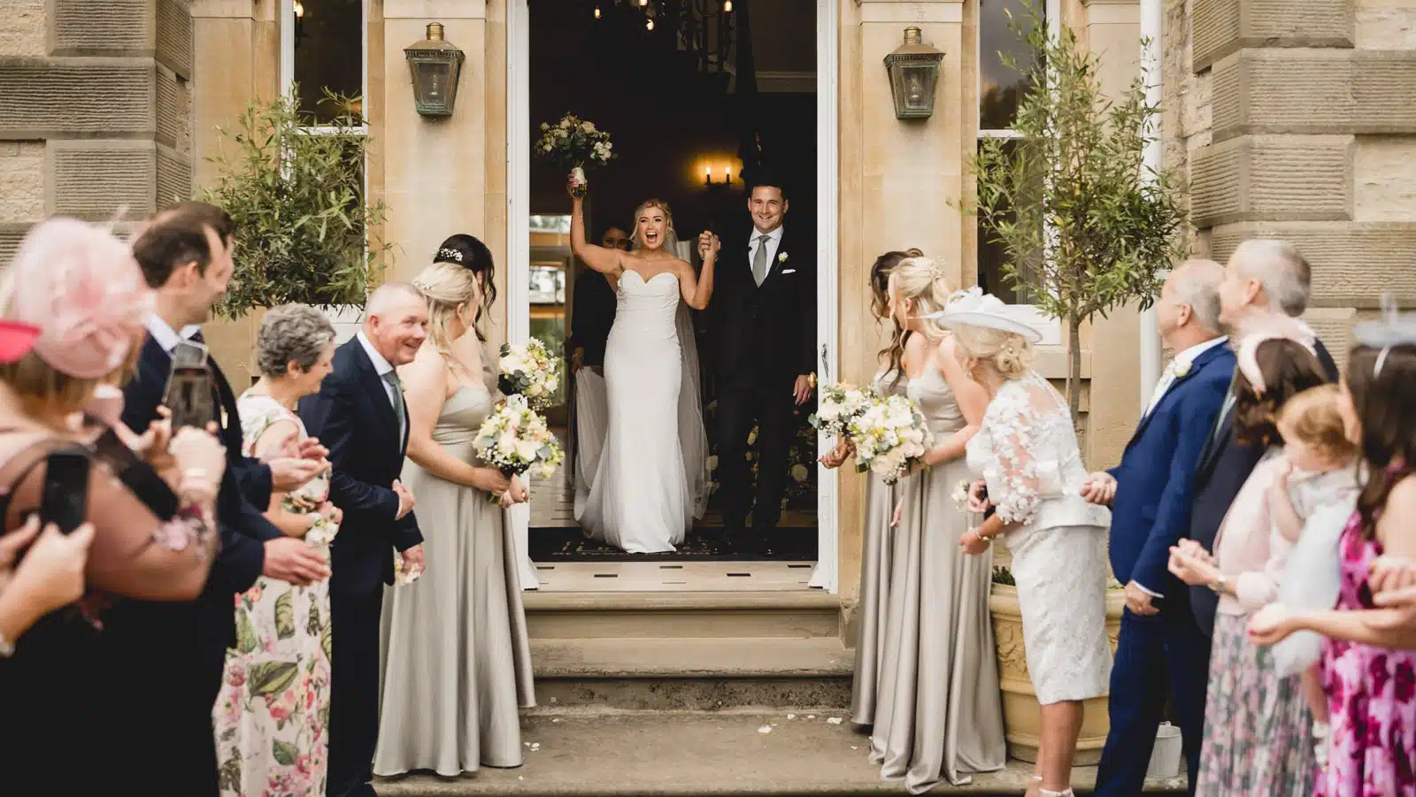 Couple stepping out of the front door at St Tewdrics House to cheering guests