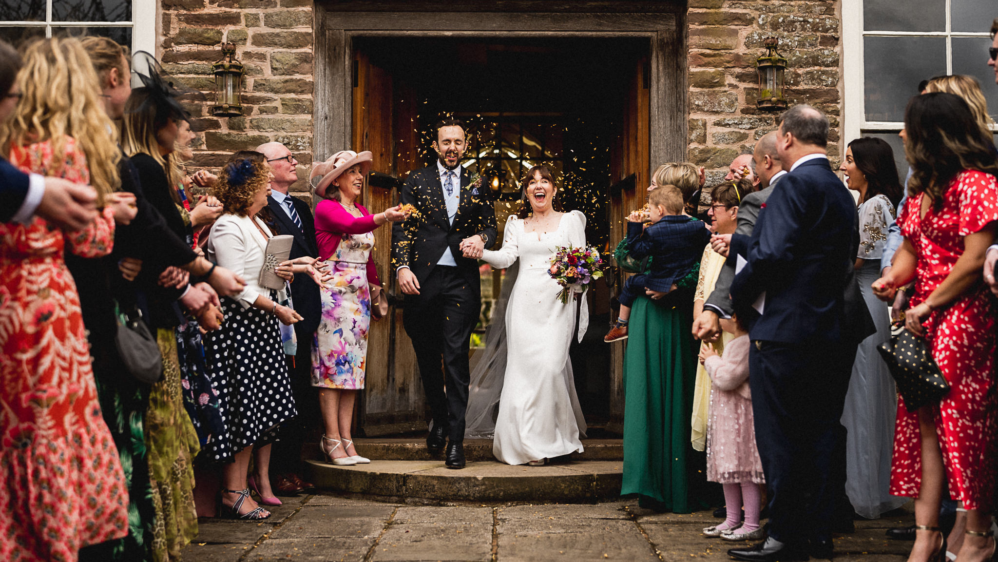 April and Alex walking out of the barn at Dewsall Court through confetti