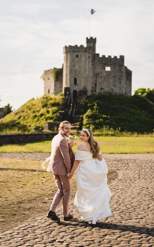 Bride and groom looking back as they run towards Cardiff Castle