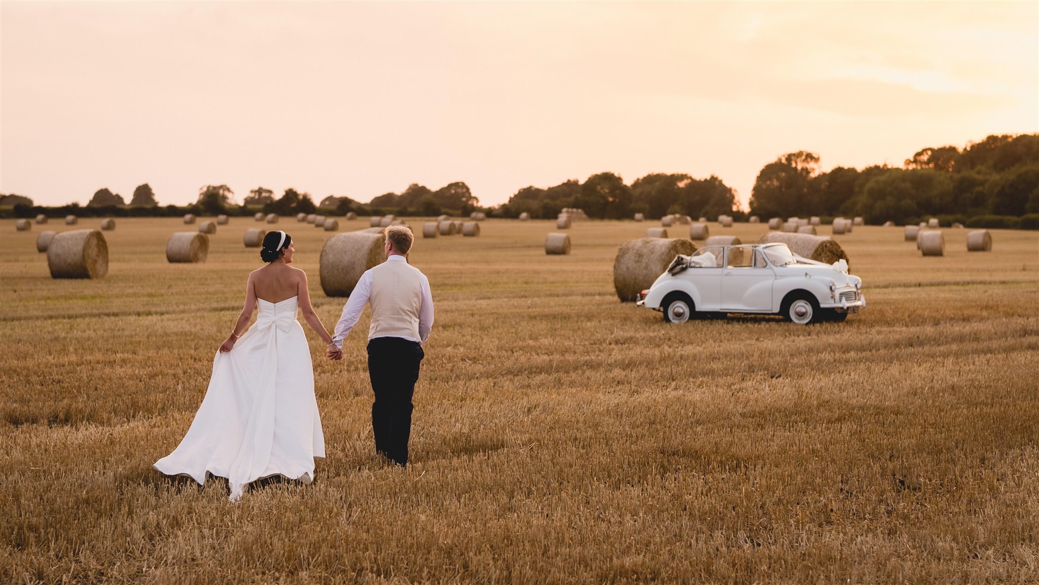 Couple walking through a harvested field towards a vintage car