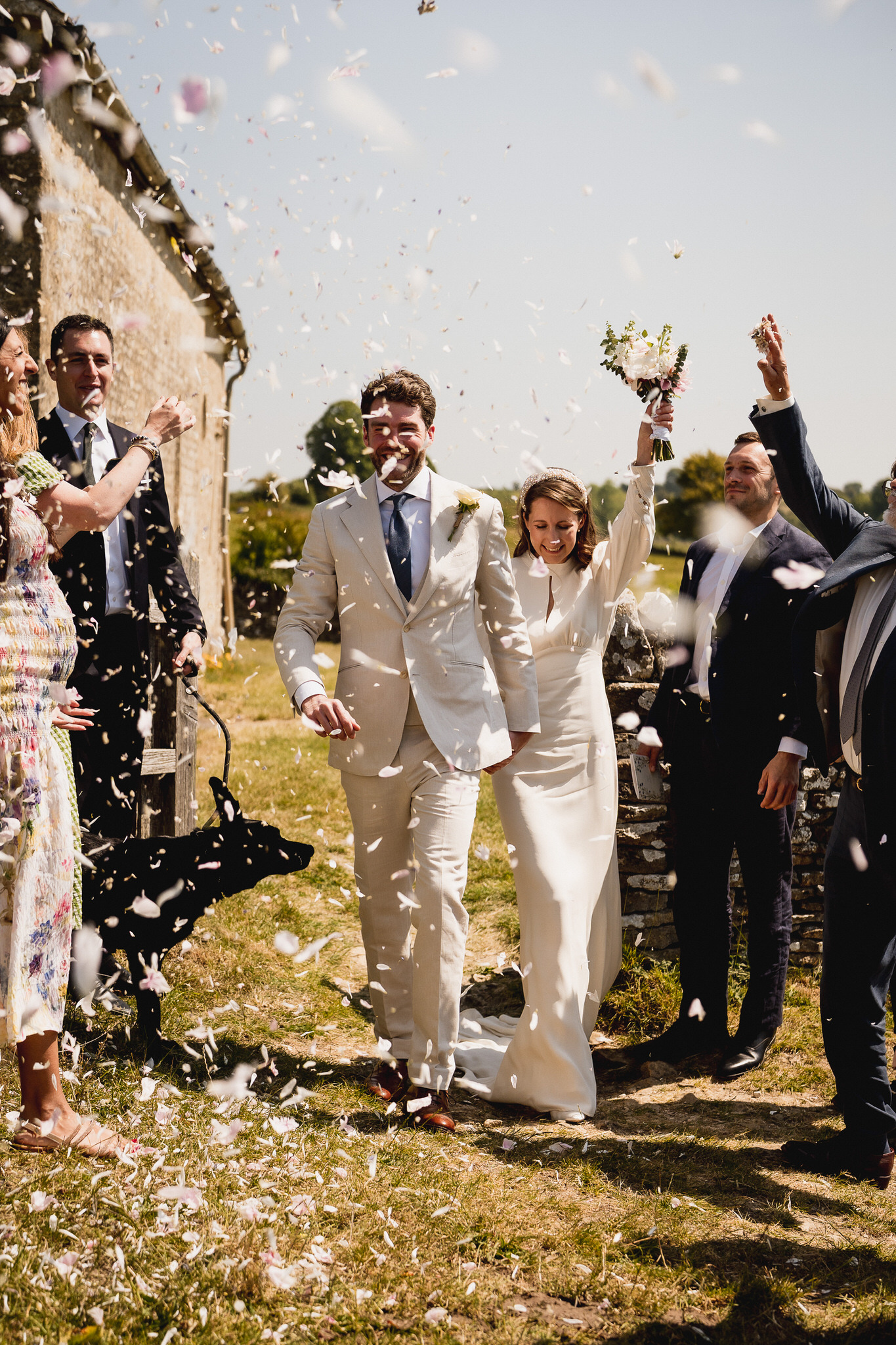 Couple laughing as confetti falls outside the church at Swinbrook