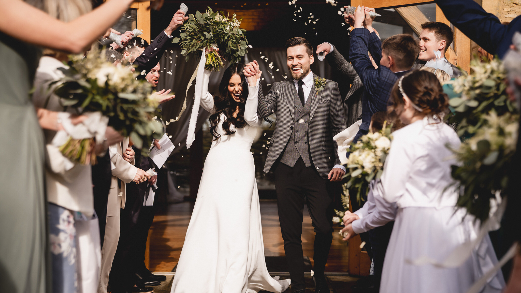 Abigail and Lewys walking out of the Barn at Upcote through confetti