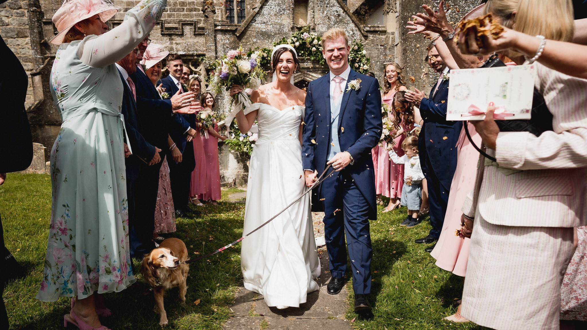 Newlyweds walking out of a Wiltshire village church through cheering guests