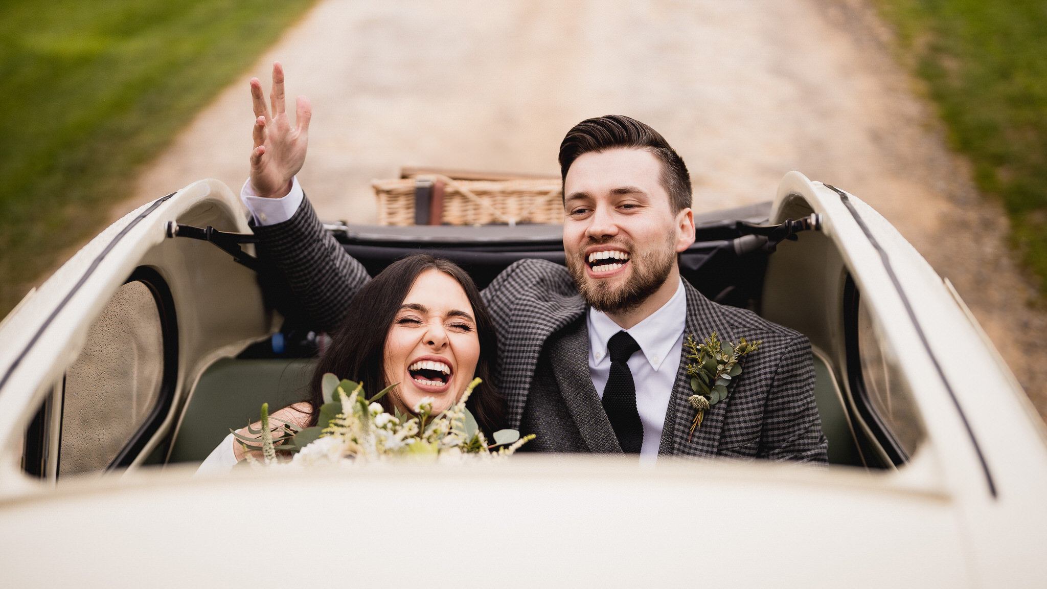 Abigail and Lewys cheering from the back of a vintage car at the Barn at Upcote