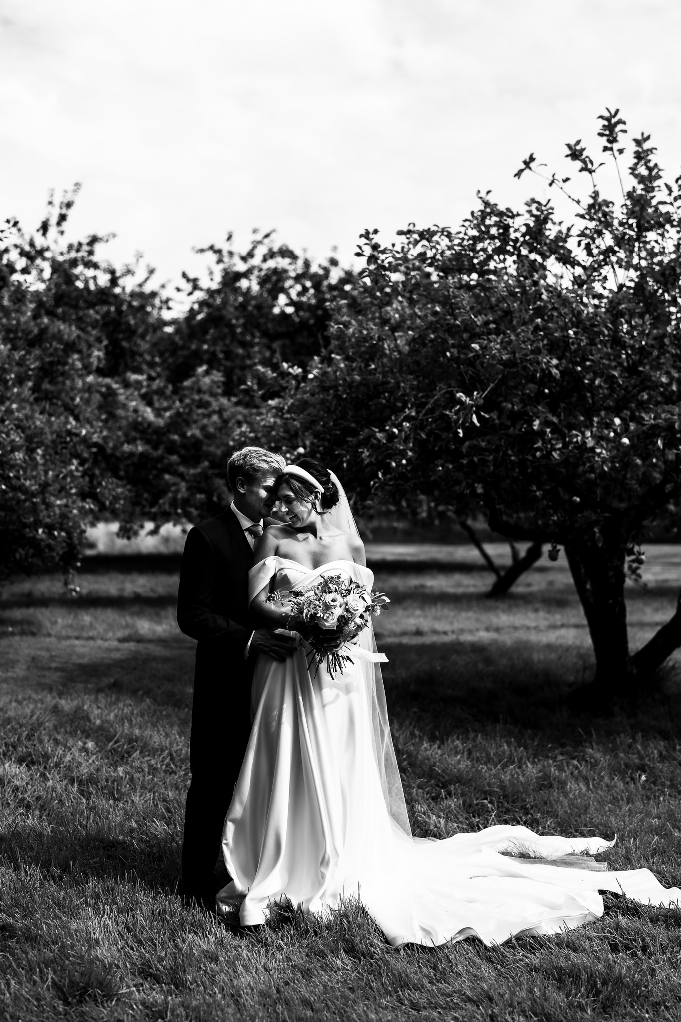 Black and white photograph of a couple embracing in an orchard beside their tipi