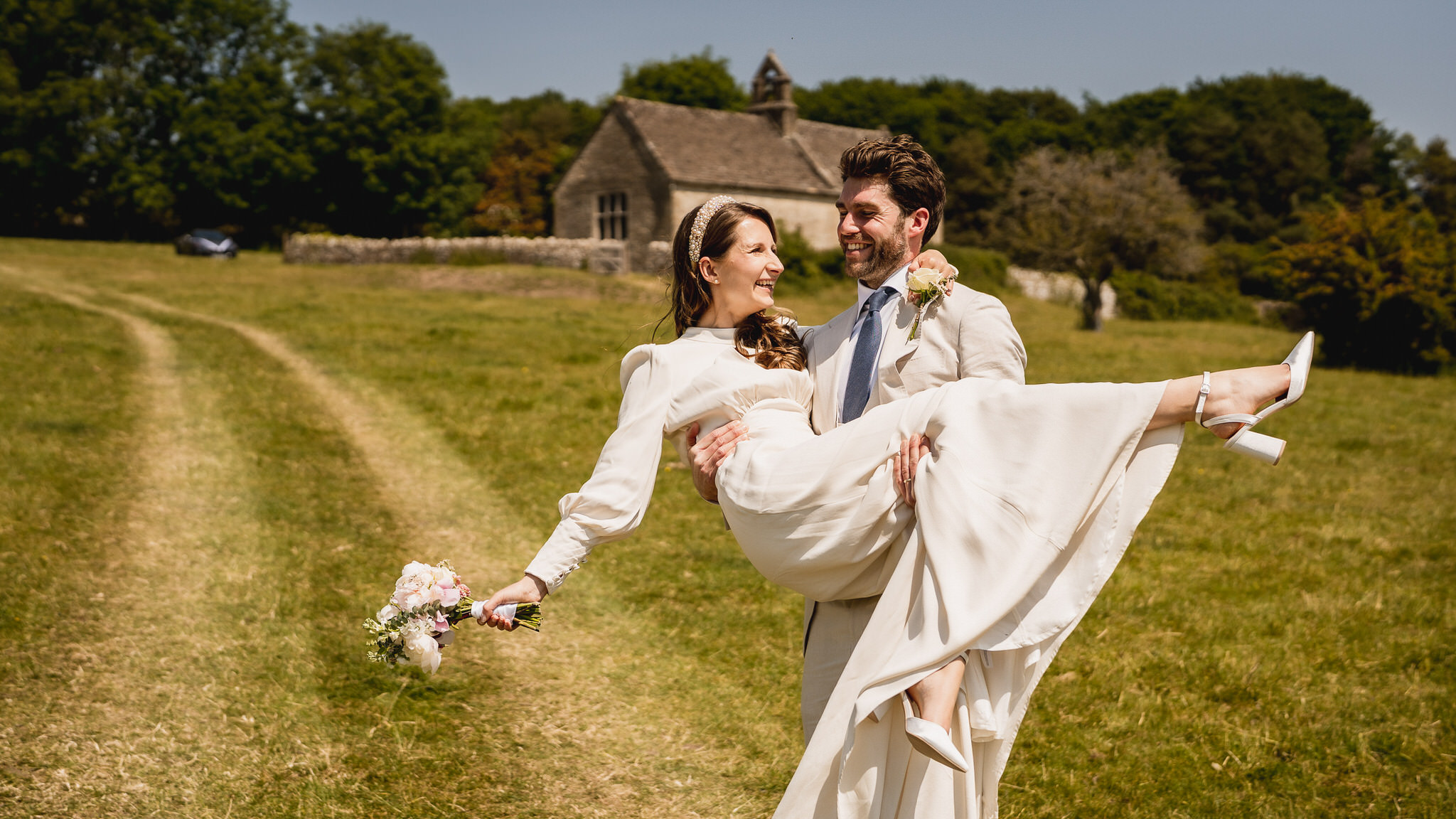 Groom lifting his bride in a meadow beside St Mary’s church, Swinbrook