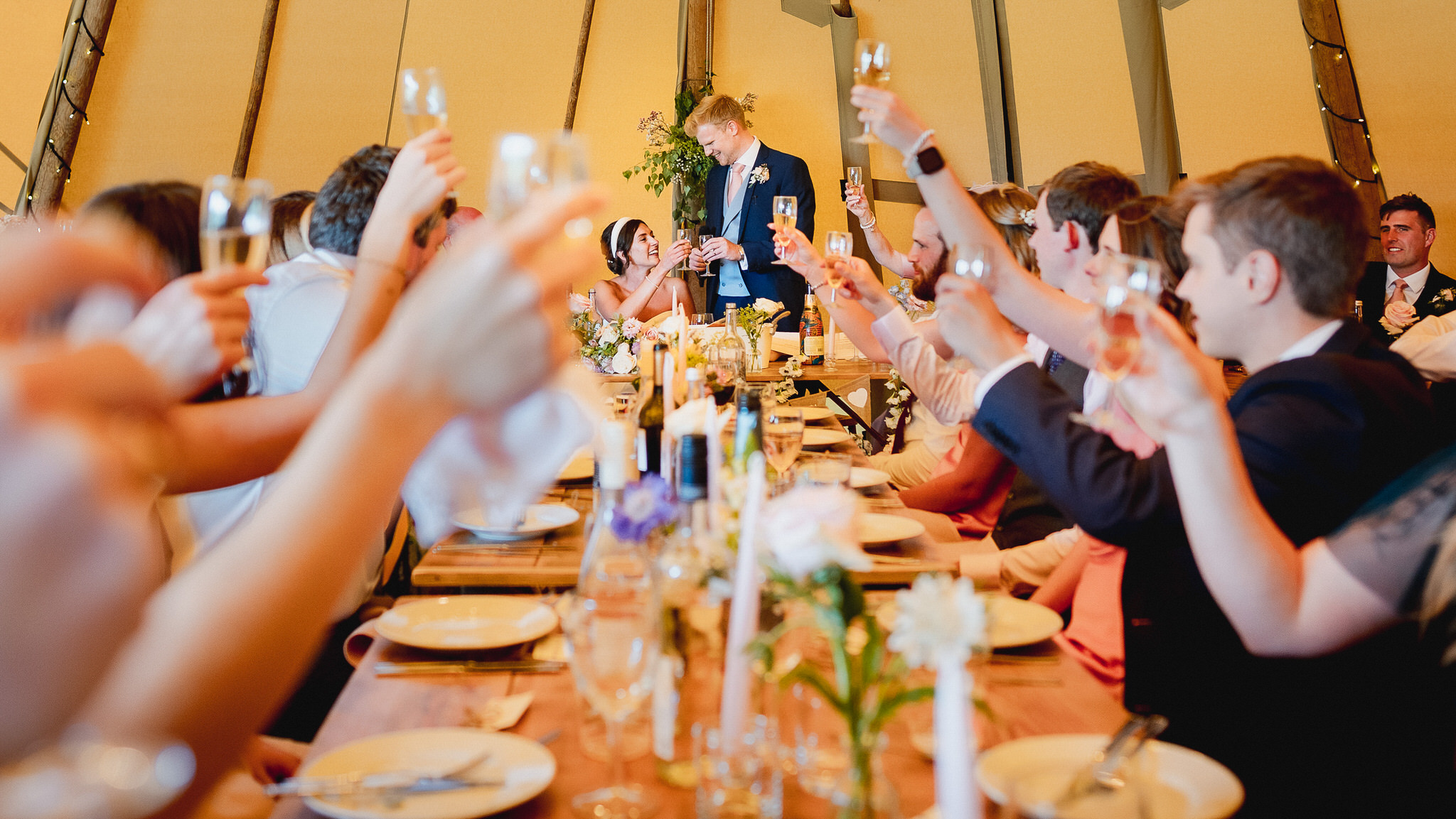 Guests raising glasses along a long table inside a tipi in Wiltshire