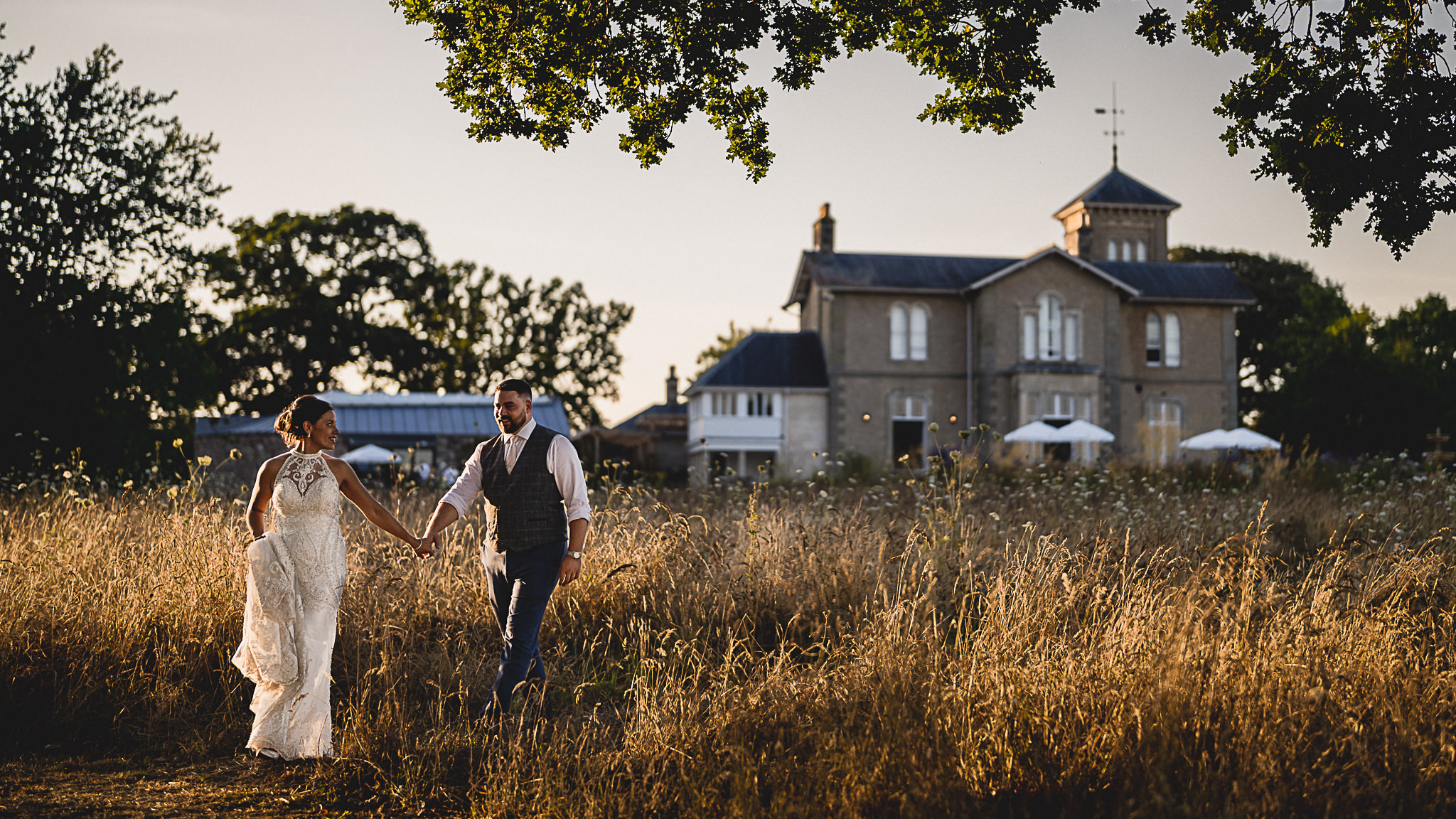 Couple walking through long grass with St Tewdrics House behind them