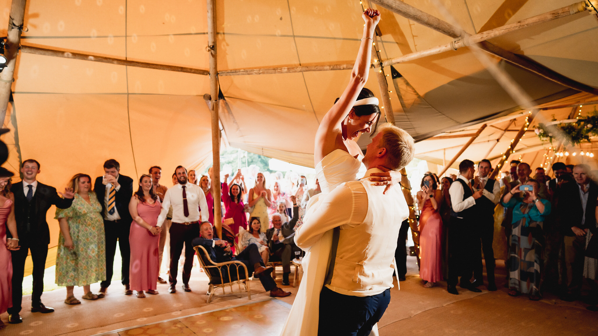 Groom lifting his bride on the dance floor inside a Wiltshire tipi as guests cheer