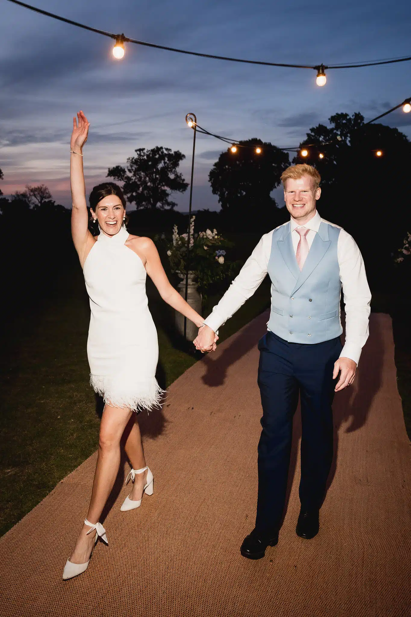 Bride and groom walking out under festoon lights at dusk