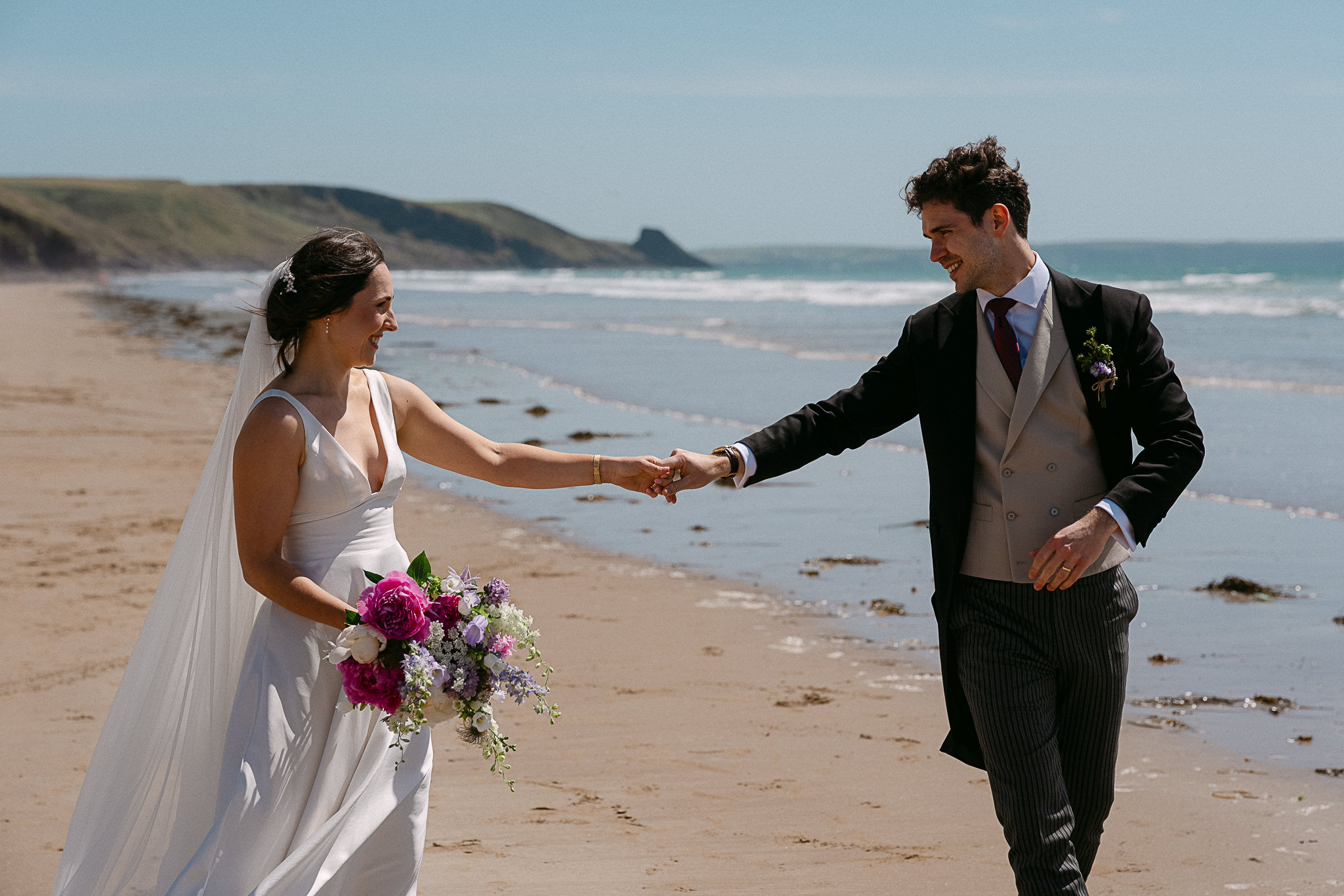 Couple walking hand in hand along the shoreline at Nolton Coast