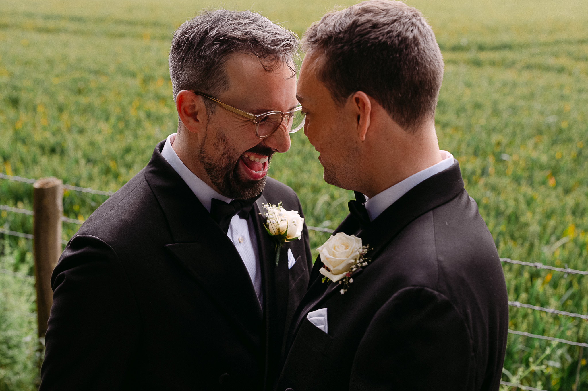 Two grooms laughing together in a field