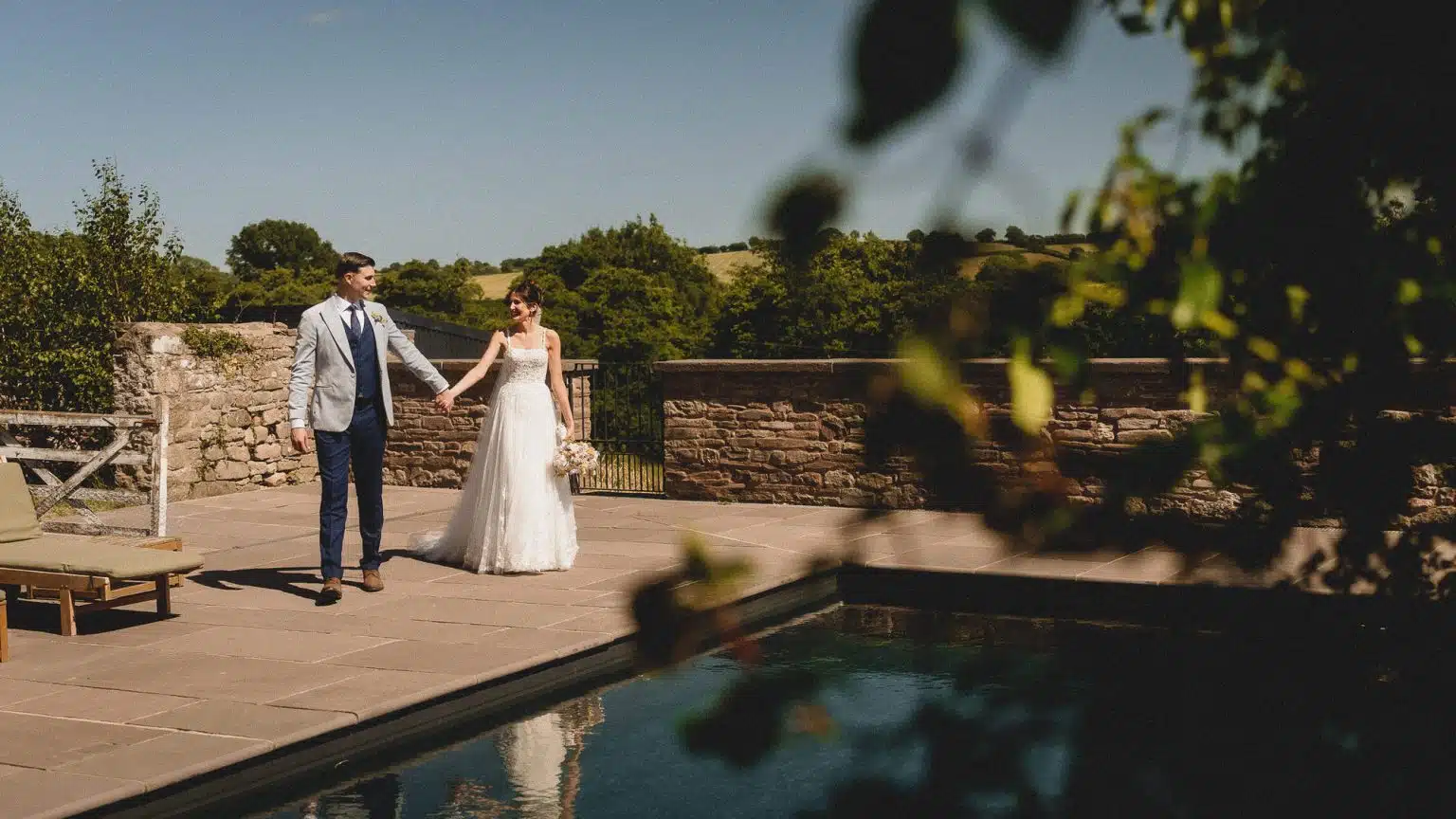 Bride and groom walking hand in hand beside the pool at Llantilio House