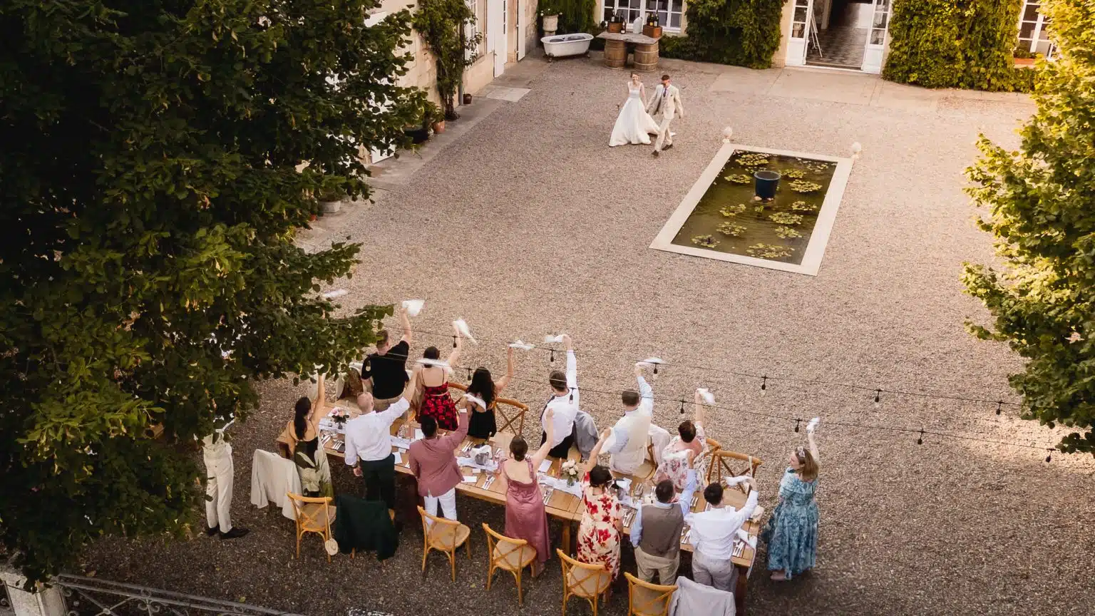 Guests waving napkins as the couple arrive at an outdoor courtyard dinner