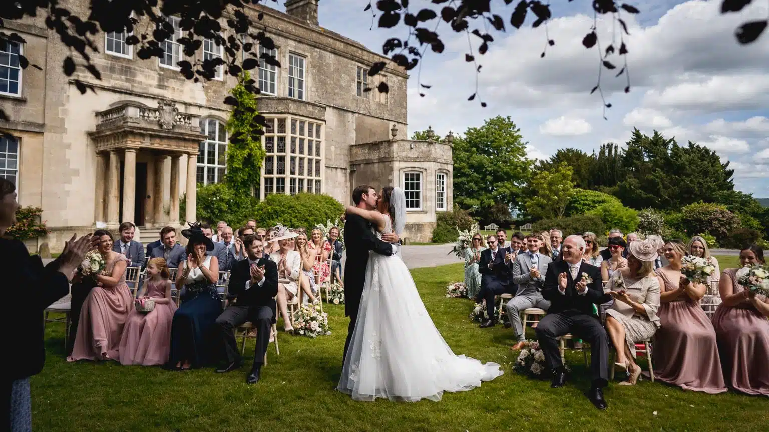 Guests applauding as the couple share their first kiss at an outdoor ceremony at Elmore Court