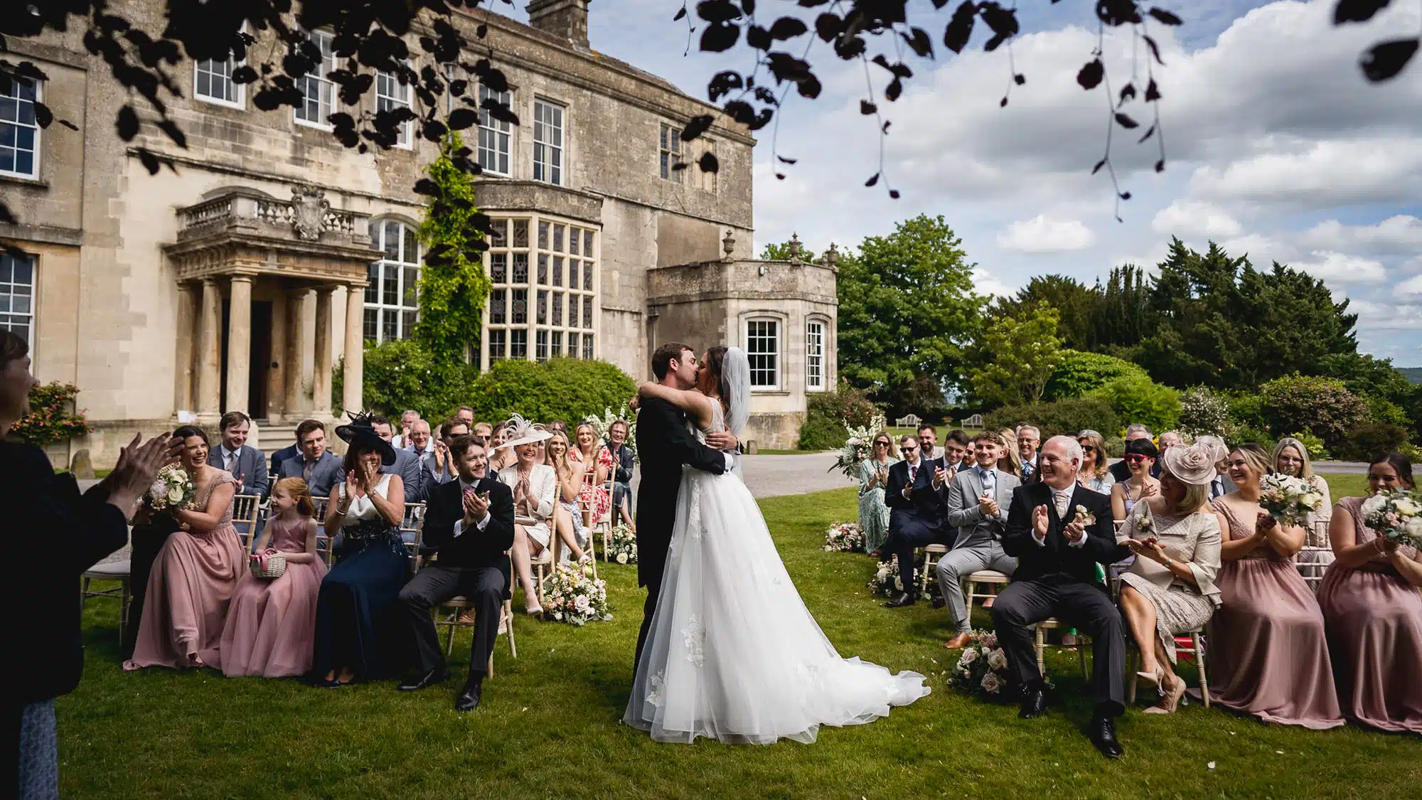Guests applauding as the couple share their first kiss at an outdoor ceremony at Elmore Court