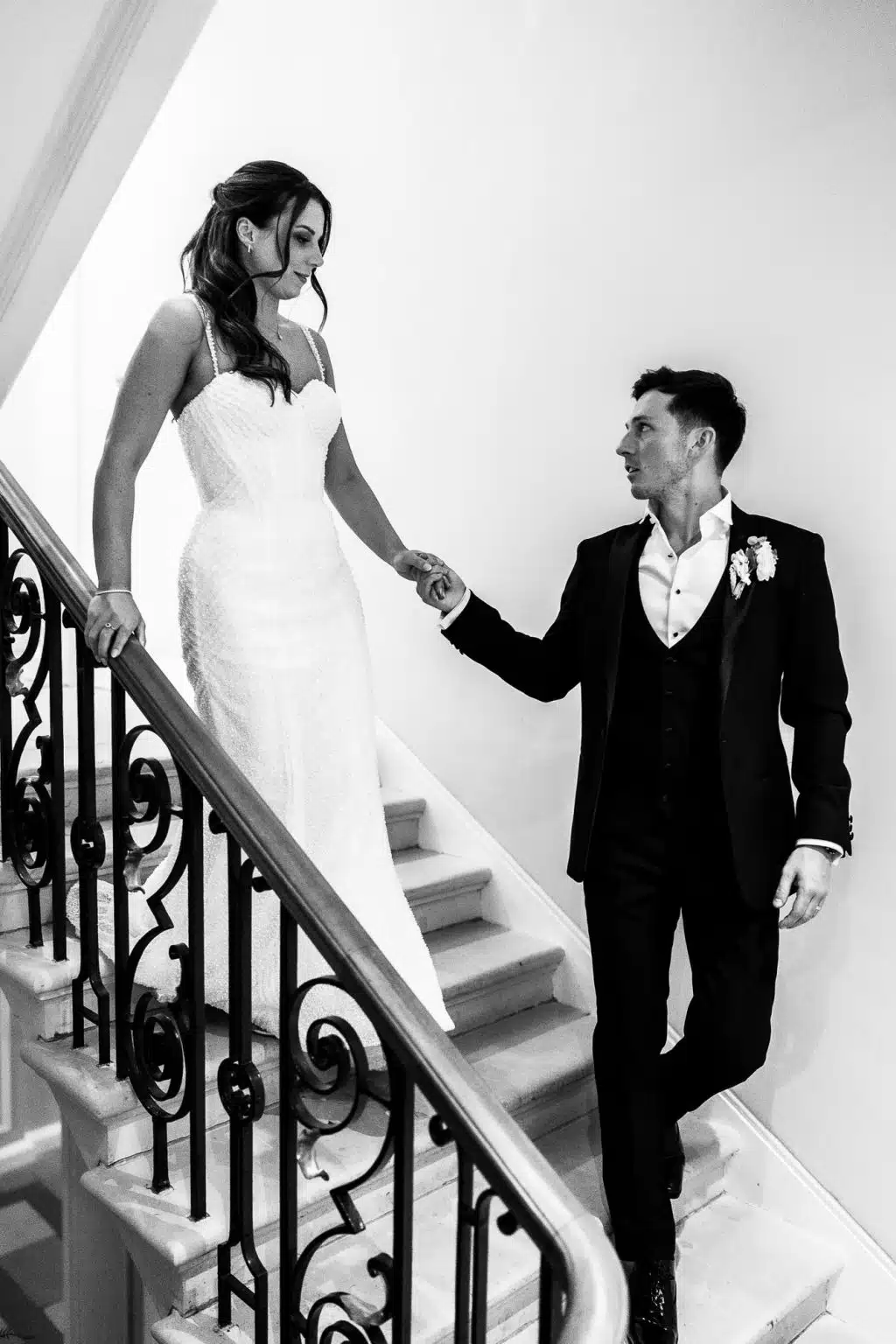 Bride and groom holding hands on a grand staircase at Sant Ffraed House