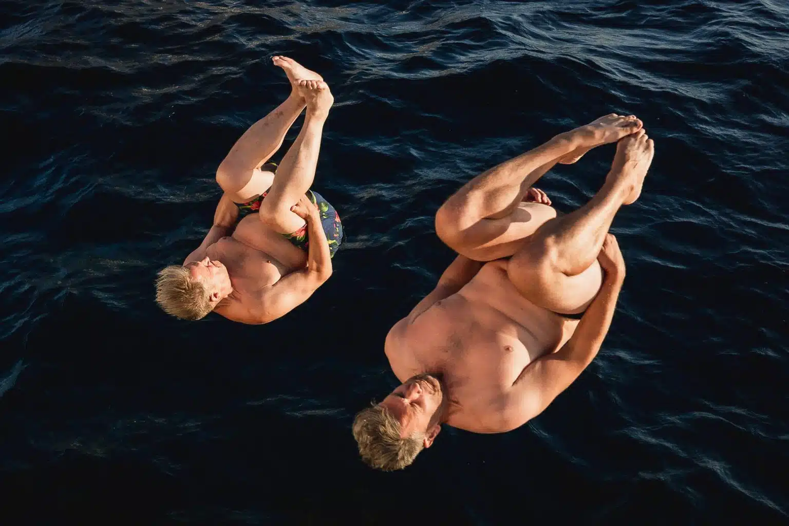 Two wedding guests mid-somersault above the sea in Santorini
