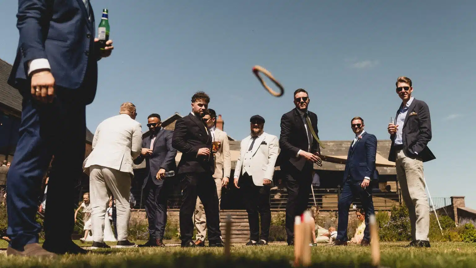 Wedding guests in suits watching a ring toss game on a sunny lawn