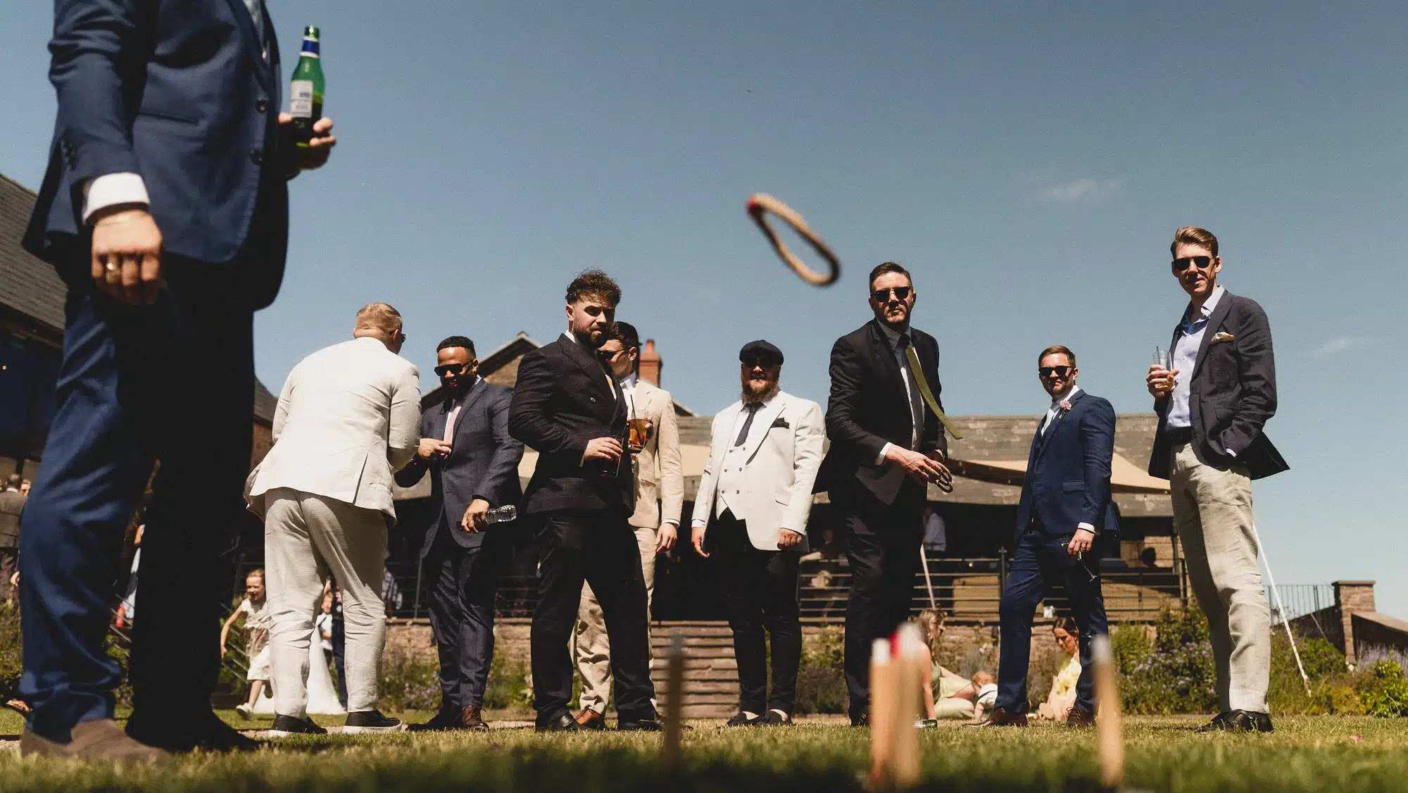 Guests watching a ring toss game on the lawn in the afternoon sun