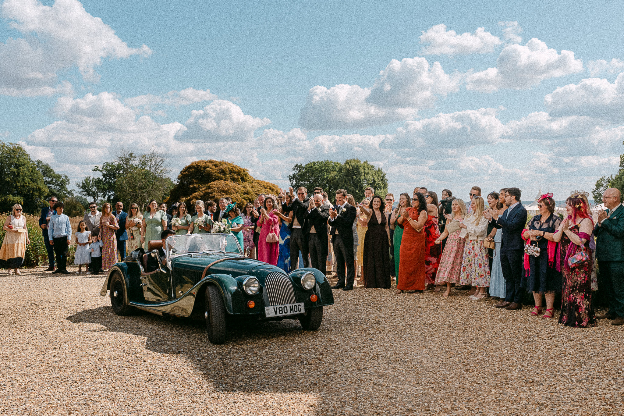 Guests cheering as the newlyweds drive off in a green Morgan