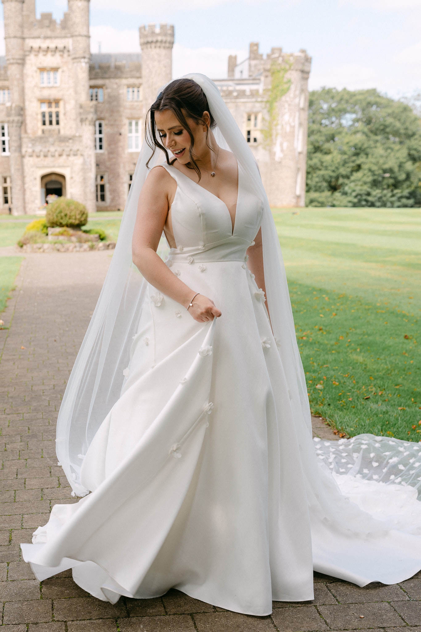 Bride holding her skirt on the lawn in front of Hensol Castle