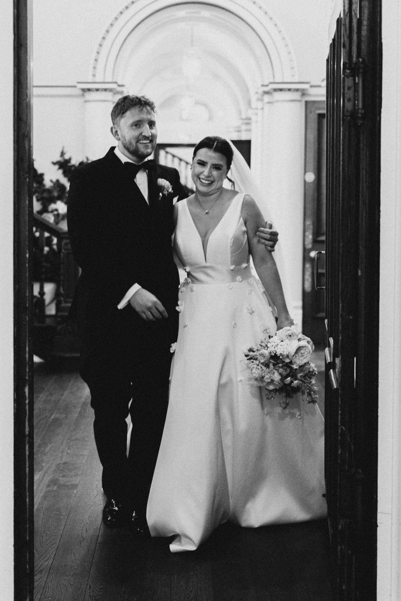 Jodie and Ieuan walking out through the castle doorway, in black and white