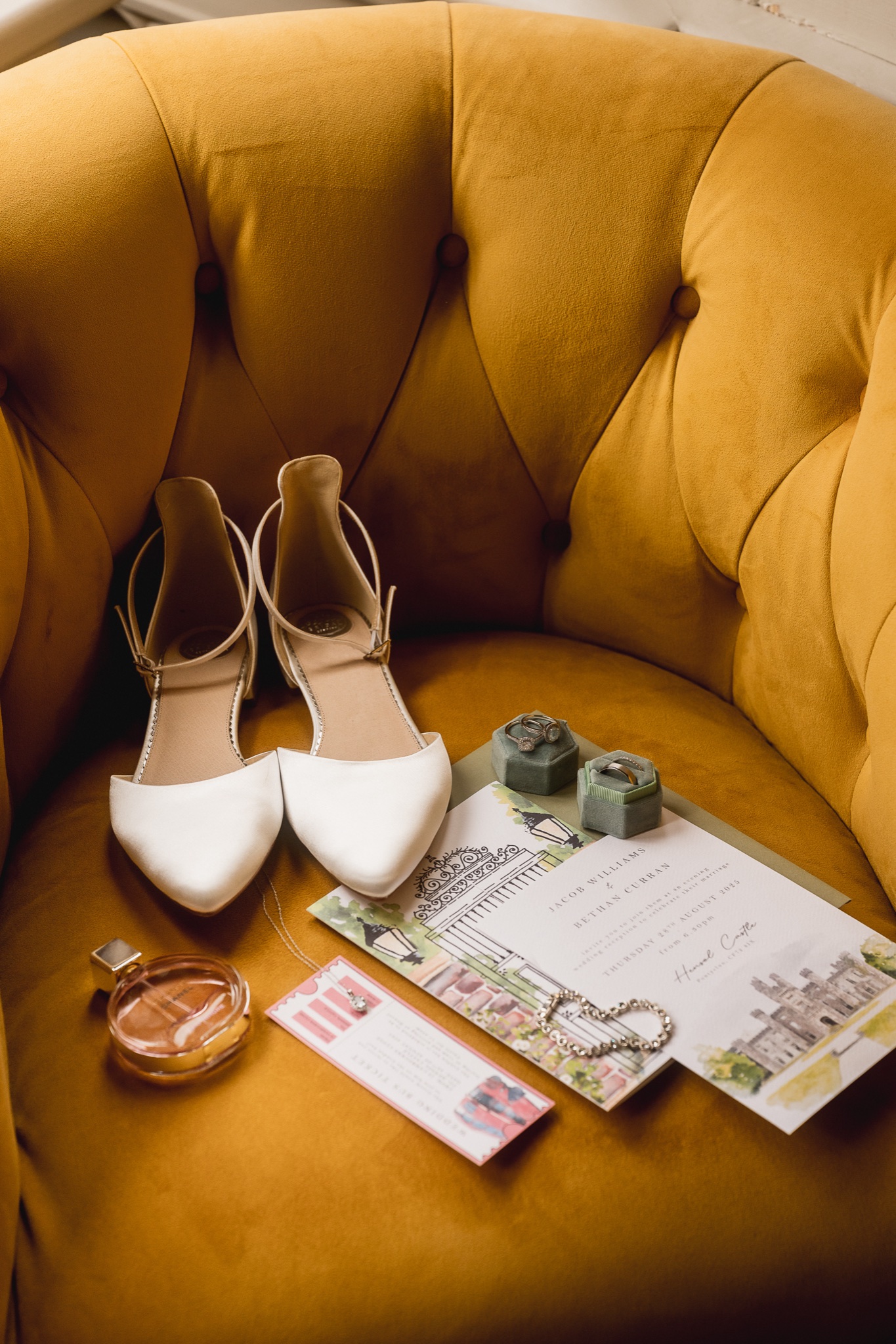 Bride’s shoes, perfume and invitation on a velvet chair