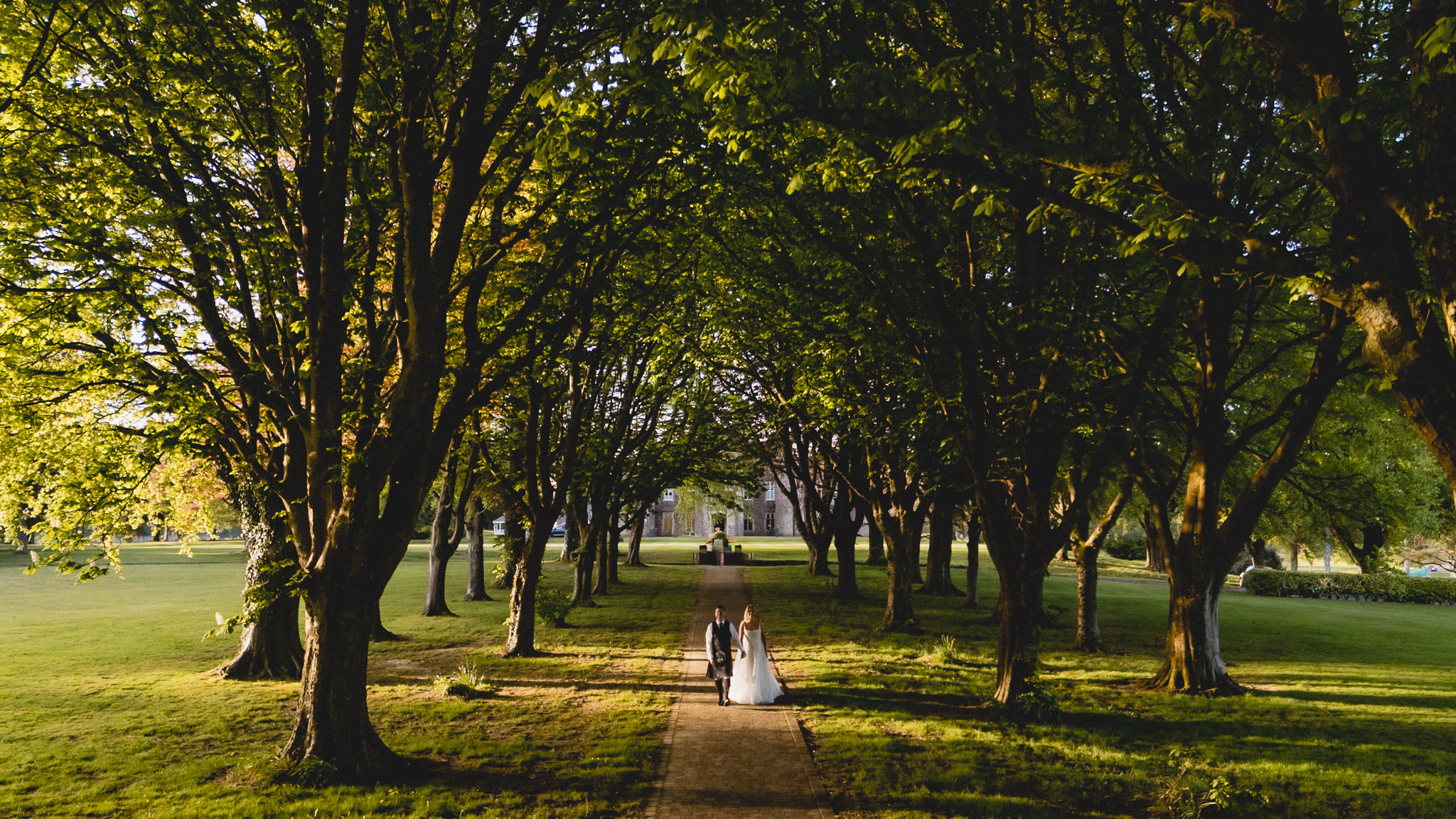 Sarah and Jamie walking the avenue of trees at Hensol Castle in the evening light