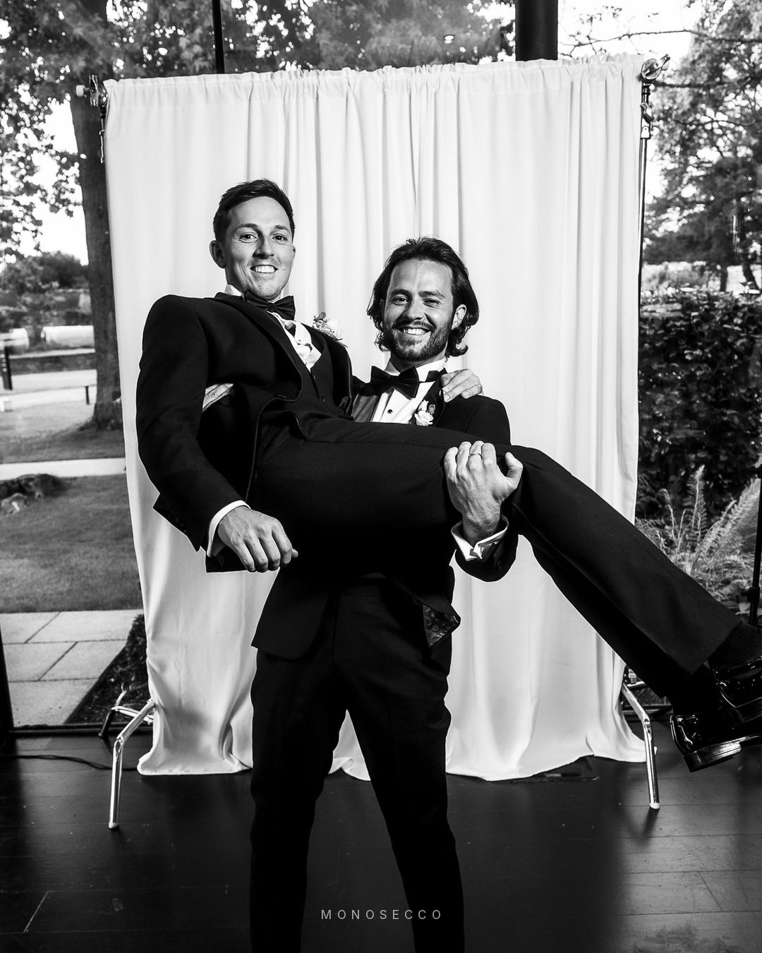 A guest lifting the groom off his feet in front of the backdrop