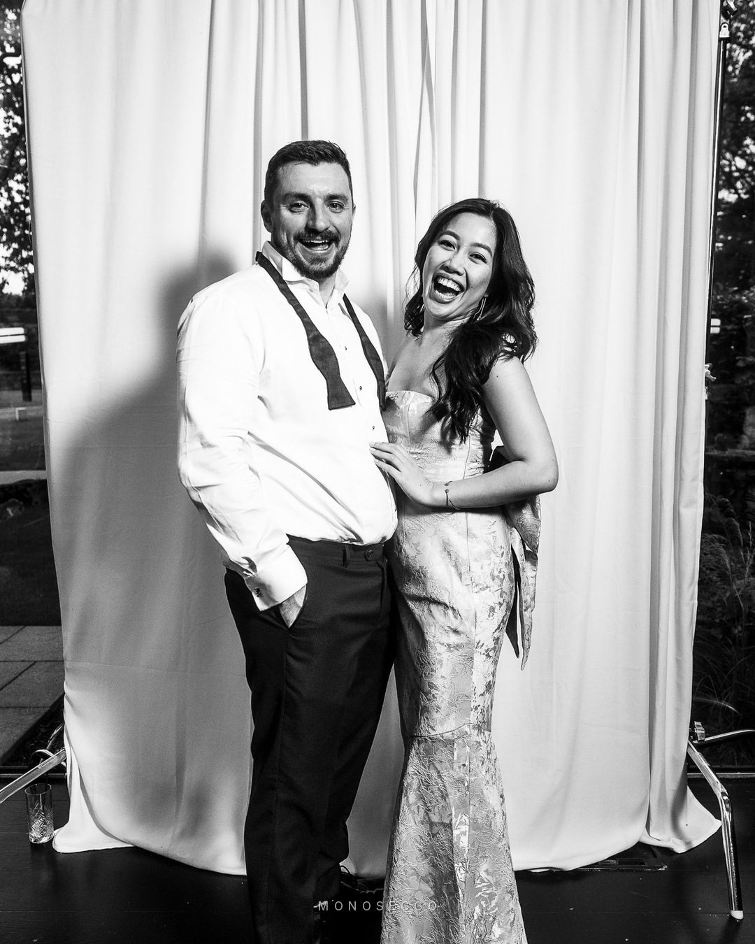 A couple laughing together in front of a white curtain backdrop