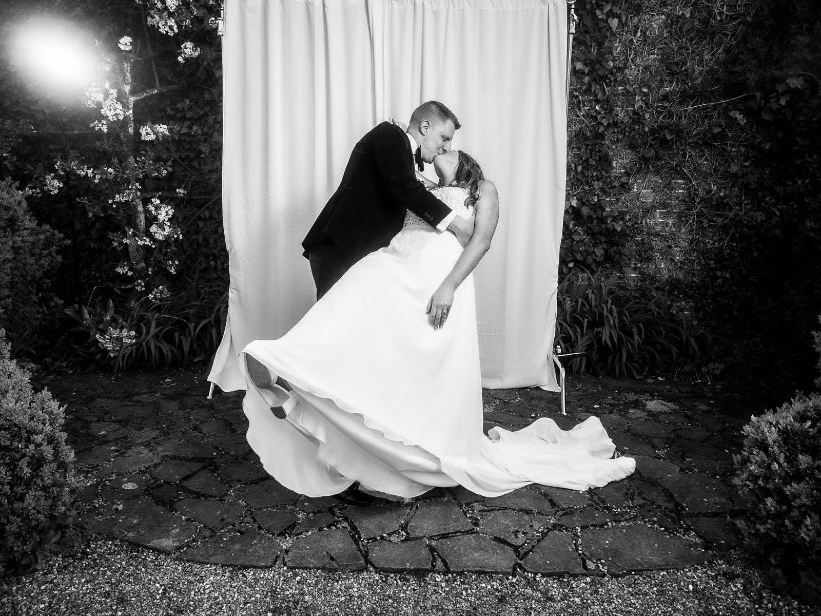 Groom dipping the bride for a kiss in front of the backdrop in a garden at night