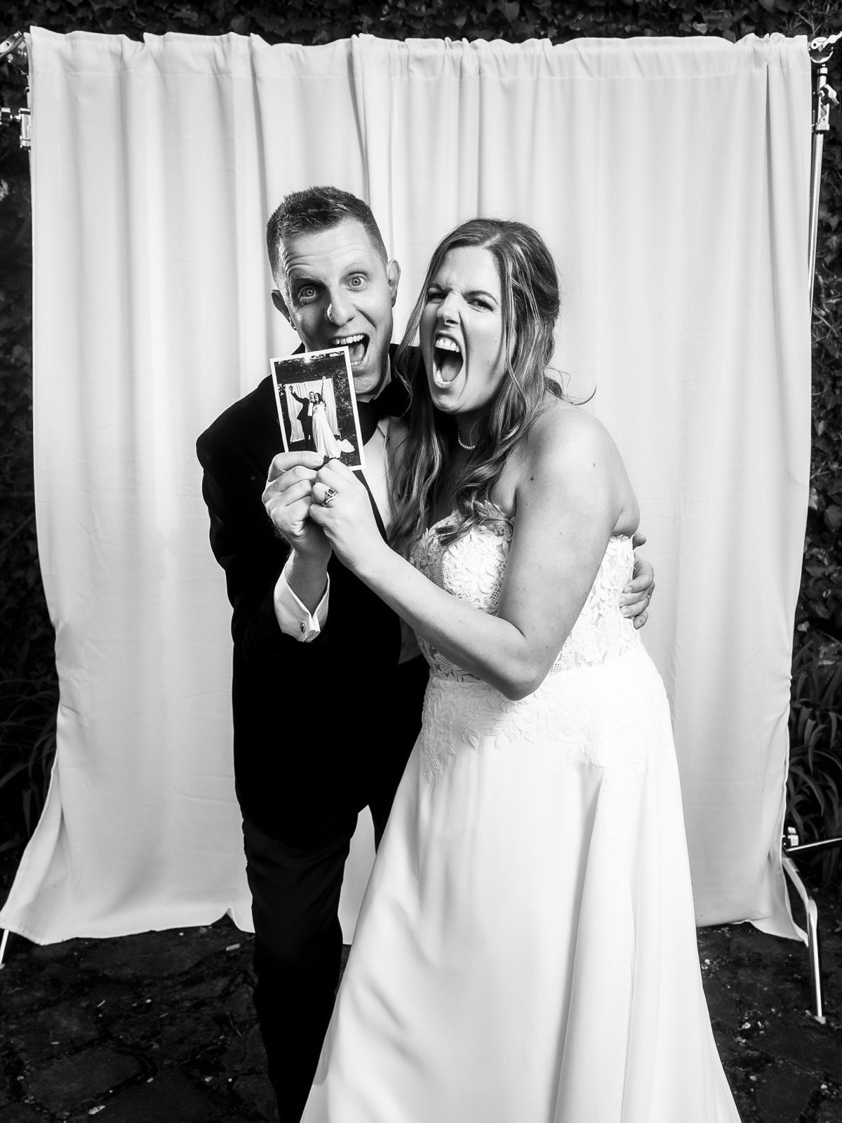 Bride and groom pulling faces as they hold up a photograph