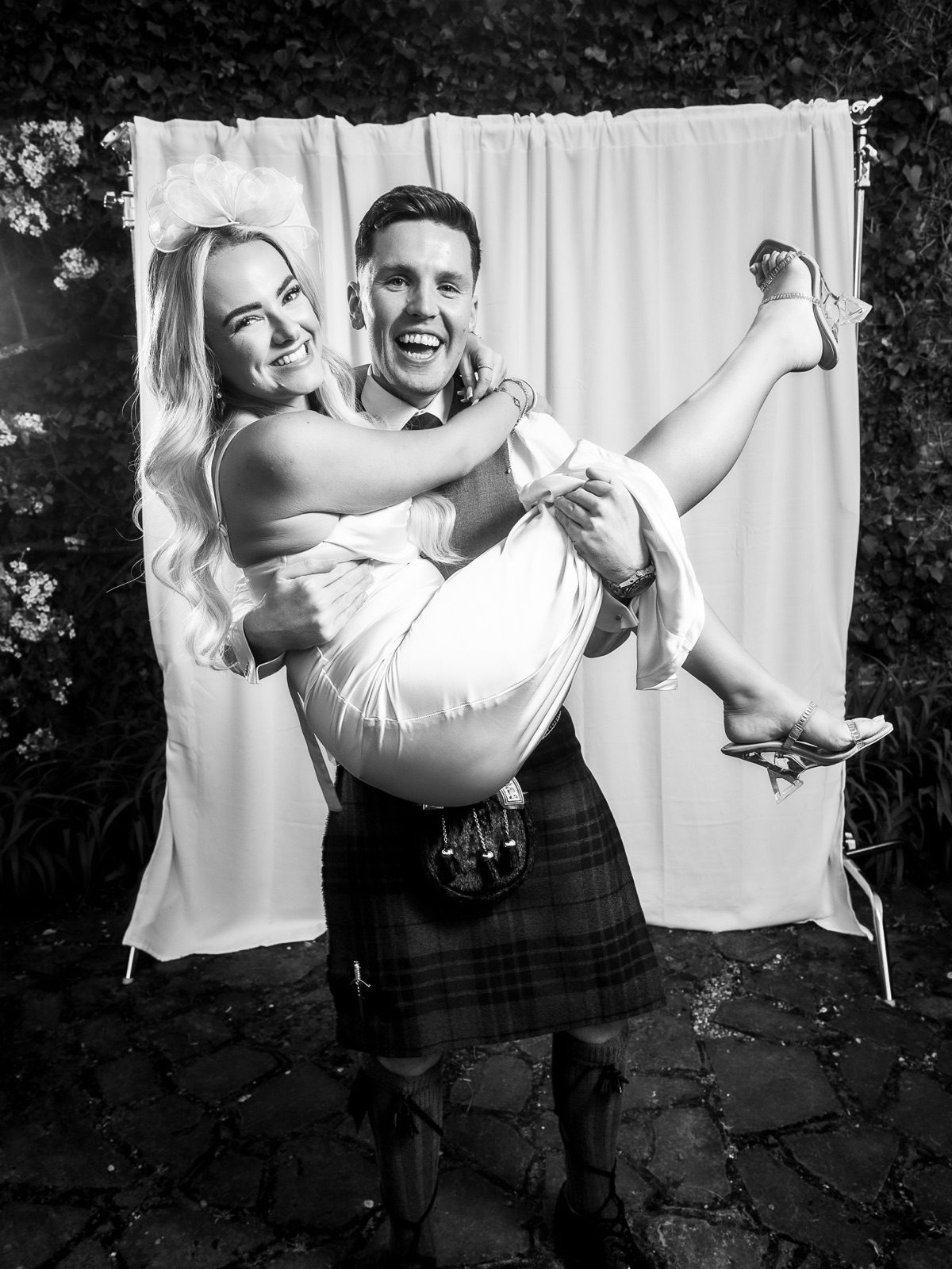 A man in a kilt carrying a laughing guest in his arms