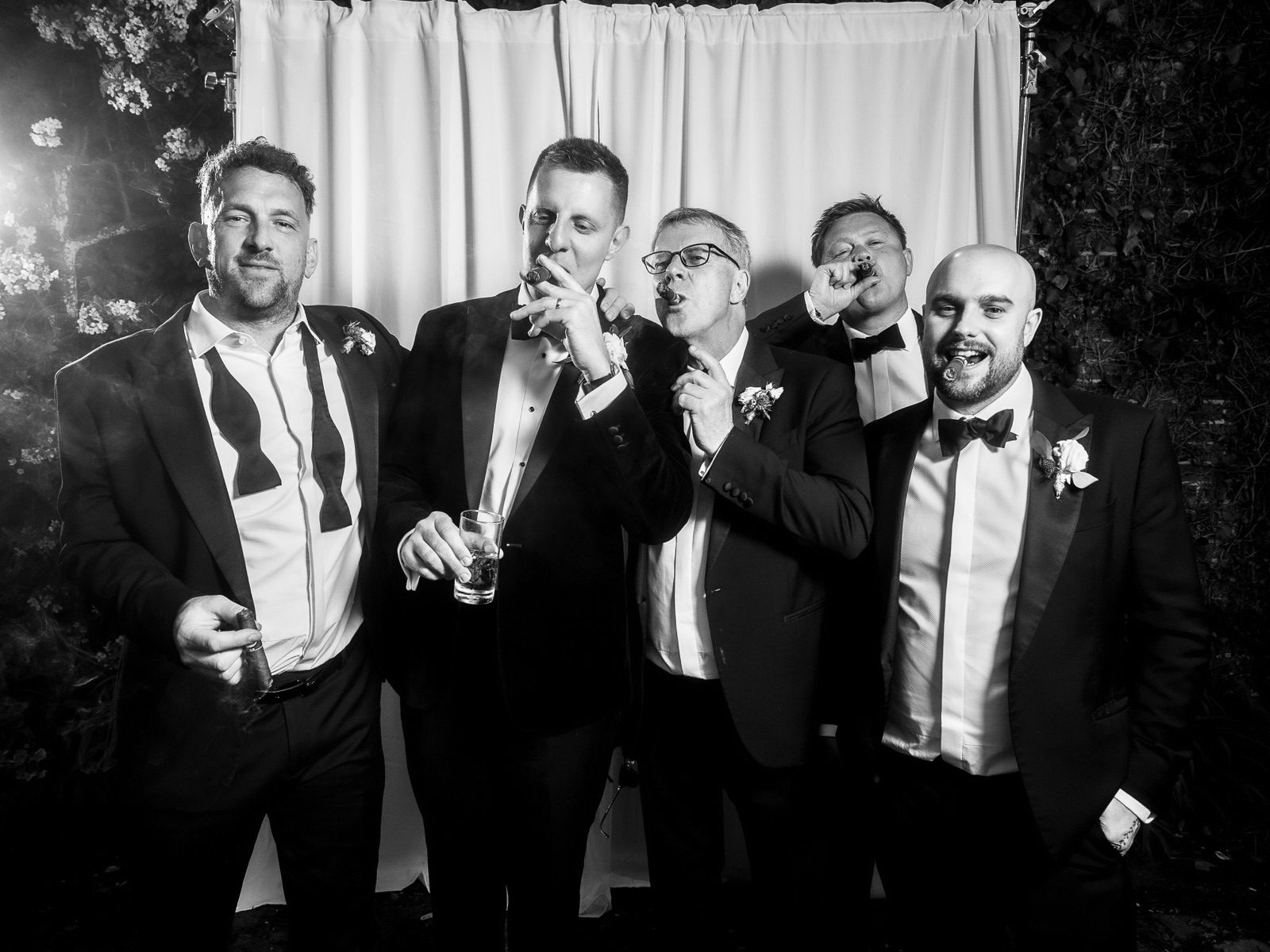 Groomsmen in black tie laughing in front of the backdrop
