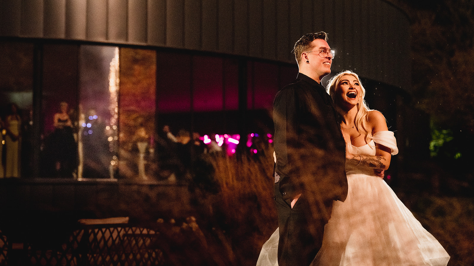 Karrie and Rafe laughing outside the glowing reception room at night