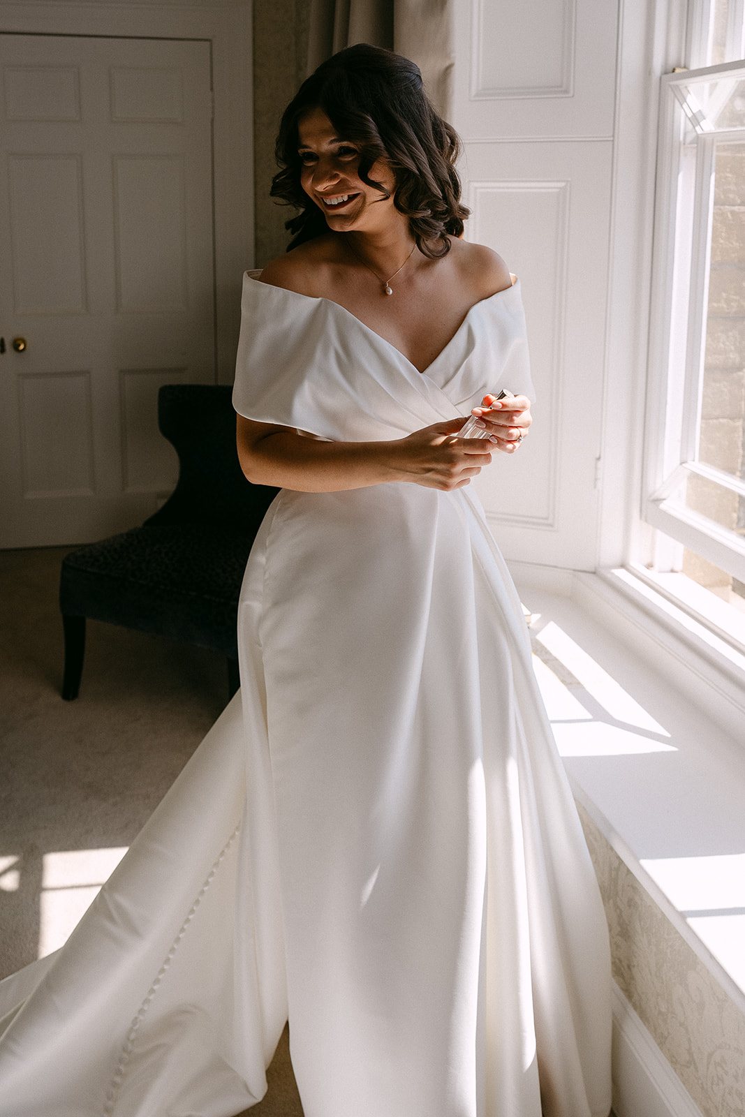 Jess in her dress by the tall bedroom window on the wedding morning