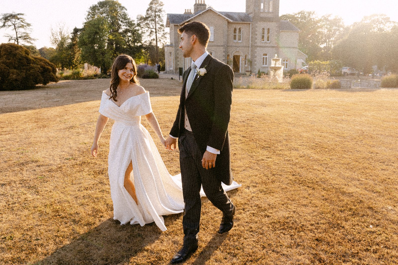 Jess and Tom walking through the golden meadow with the house behind