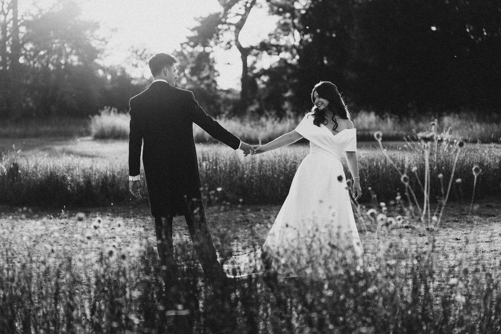 Jess and Tom holding hands in the long grass, in black and white