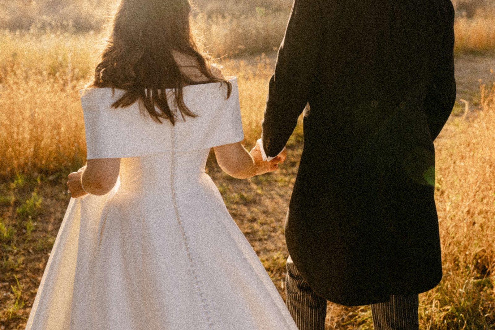 Jess and Tom walking hand in hand through golden grass